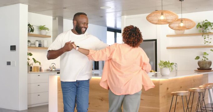 African American couple taking hands and laughing, dancing around kitchen island, celebrating love