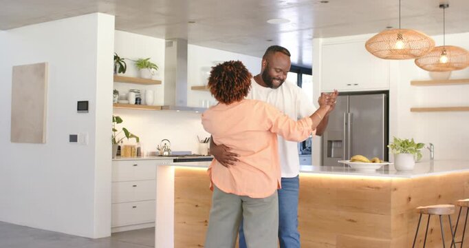 African American couple wrapping arm holding hand swaying sharing tender moment near kitchen island