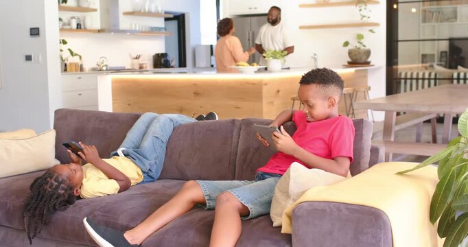 African American parents starting snack prep and talking while children scrolling devices on couch