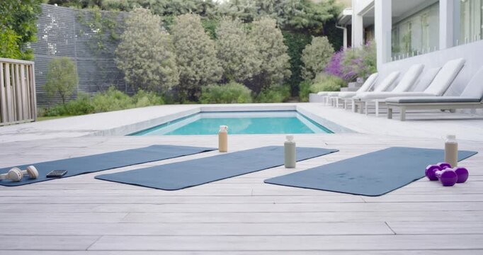 Camera is sliding left, three blue yoga mats are holding bottles on wooden deck for workout