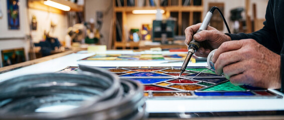 Fototapeta premium Artisan soldering a colorful stained glass panel in a workshop with skilled hands