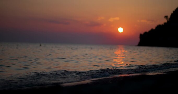 Sunset over calm sea with gentle waves lapping a sandy beach and silhouetted coastline reflecting golden evening light