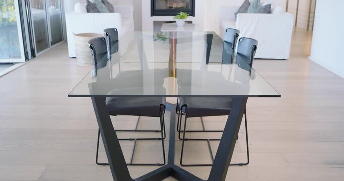 Camera pulling back glass-top table reflecting room and revealing sofas, fireplace to show layout