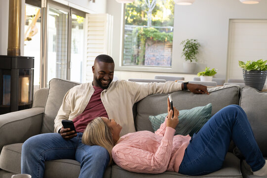Couple sitting on gray sofa in living room, man holding smartphone while woman scrolling phone
