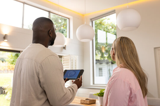 Diverse adults examining tablet with circular gauge, standing in modern dining room near windows