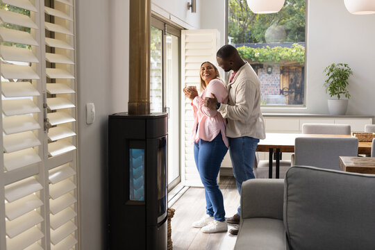 African American couple standing by glass door in open-plan home, woman holding mug, stove visible