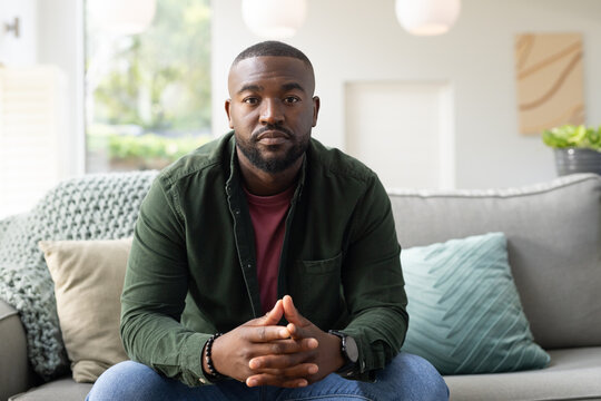 Adult African American man sitting on gray sofa in living room with beaded bracelet and pillows