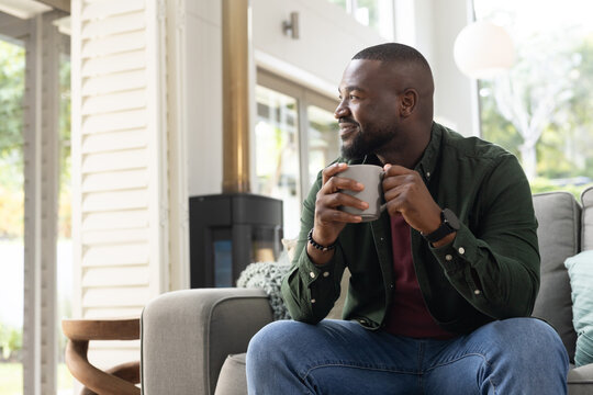 African American adult male sitting on right in living room, holding ceramic mug, copy space