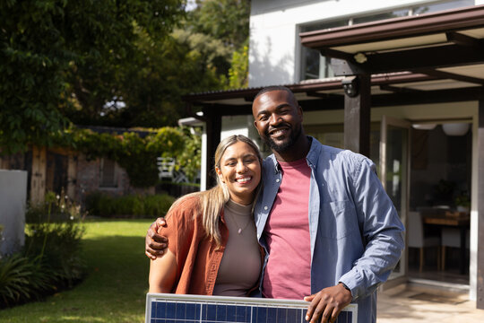 Couple standing on lawn in front of house holding solar panel near patio garden beds