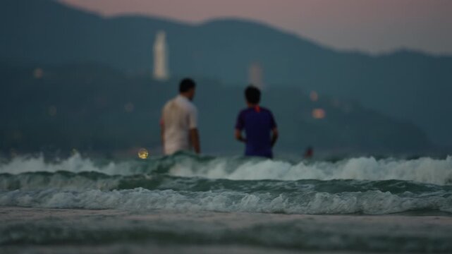 People swim in Danang sea, Lady Buddha statue and Linh Ung Pagoda above waves and tourists in Da Nang, Coastal view of Son Tra Peninsula with Buddhist landmark, mountains and ocean shoreline 4k