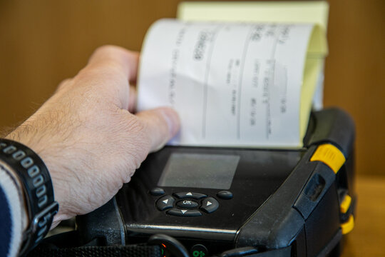 Person checking or picking up a label from a mobile printer used for printing barcode labels and receipts in a warehouse or logistics environment. The portable printer uses direct thermal printing