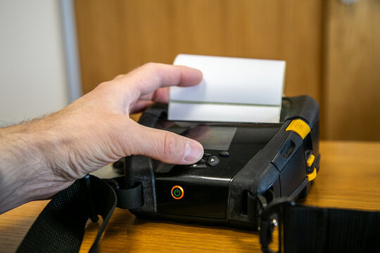 Person checking or picking up a label from a mobile printer used for printing barcode labels and receipts in a warehouse or logistics environment. The portable printer uses direct thermal printing