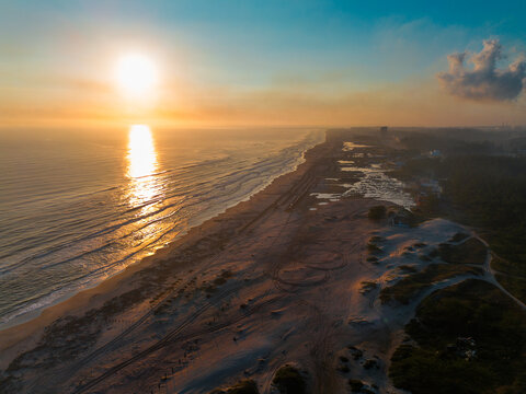 Cinematic 4K aerial drone captures Miramar Beach dunes at sunrise in Ciudad Madero, Tamaulipas, with warm orange light painting the sky and sea, palapas dotting the shoreline and ATV tracks