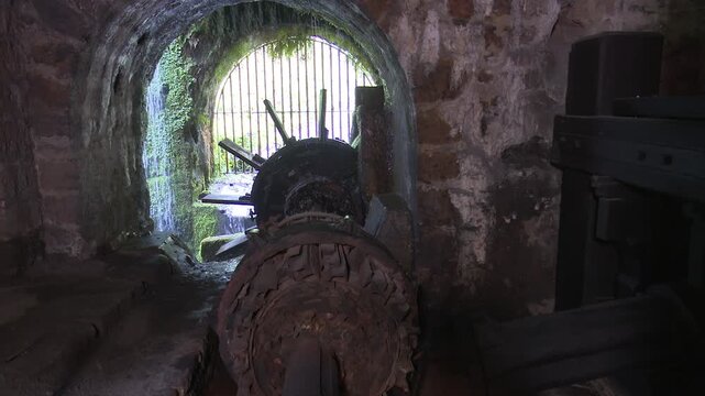 Historic water wheel inside stone tunnel with waterfall entrance view