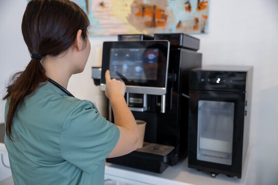 Tired female doctor making herself coffee in a hospital kitchen