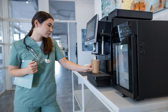 Tired female doctor making herself coffee in a hospital kitchen