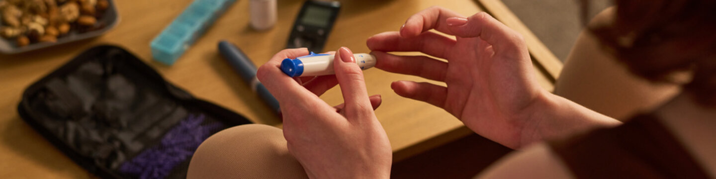 Close up of young woman checking blood glucose with lancet device at home, managing diabetes during pregnancy. Useful for healthcare