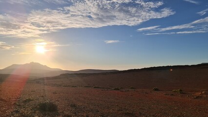 Naklejka premium Reddish Desert Plain with Glowing Sun and Hazy Mountain Silhouette