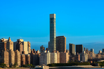 Obraz premium High rise buildings in the Sutton Place neighborhood stand beside the East Midtown Greenway with the iconic Queensborough Bridge visible on the side in New York City.