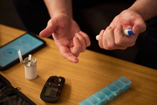 Close up of middle aged man checking blood sugar with lancet device and glucose meter at home, managing diabetes. Useful for healthcare, chronic disease management, home monitoring