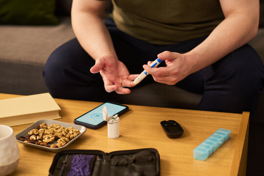 Middle aged man checking blood sugar with lancet device and glucose monitor at home, managing diabetes and treatment routine. Close up for healthcare app, telemedicine, patient education
