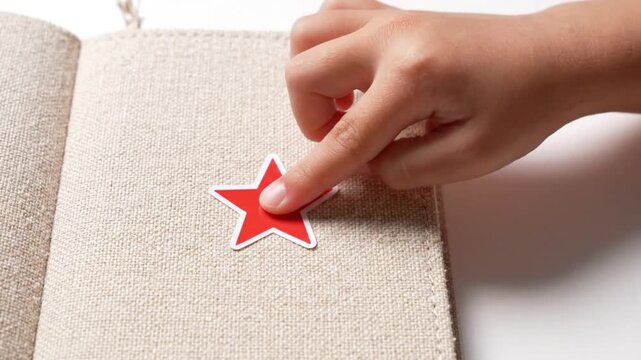 A hand placing a red star sticker into a book on a table in a home office video