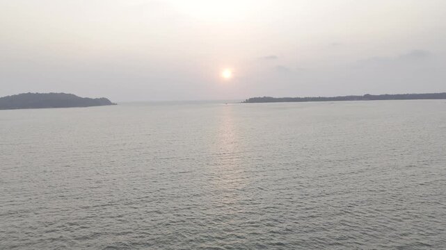 Aerial shot of sunset over the Chapora River in Goa, framed by two rugged coastal cliffs, with warm evening light reflecting on the water and highlighting the region's dramatic tropical landscape.