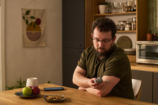 Middle aged man checking glucose monitor and insulin device at home, managing diabetes and daily treatment. Useful for healthcare, chronic condition, home care marketing