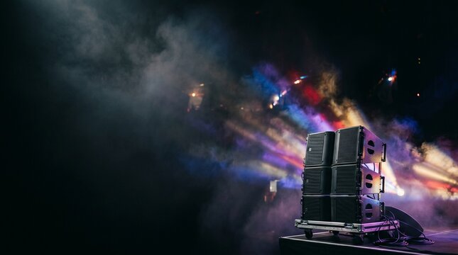 Concert stage with stacked speakers and colorful lights in smoke