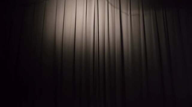 Static shot of stage curtain illuminated by overhead spotlight revealing fabric texture and haze in dark theater auditorium during rehearsal