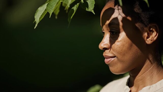 African american woman standing outdoors in natural sun light. Profile side view face portrait with tree shadow pattern on skin. Calm wellness lifestyle concept
