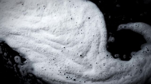 Close-up of white foam drifting on dark liquid surface