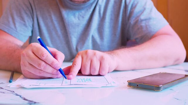 Low angle close-up of a man's hands neatly filling out a paper document.Work home office.A male  hands carefully writing on an official form or contract under soft natural light.