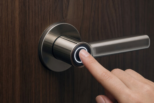 Close-up of a hand pressing an illuminated button on a modern smart door handle mounted on a dark wooden door.