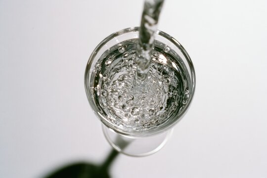 Stream of clear water filling a glass, creating ripples and bubbles