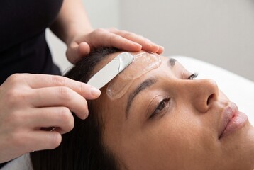 Naklejka premium Close-up of a beautician applying a clear gel mask to a woman's forehead with a spatula during a facial treatment.
