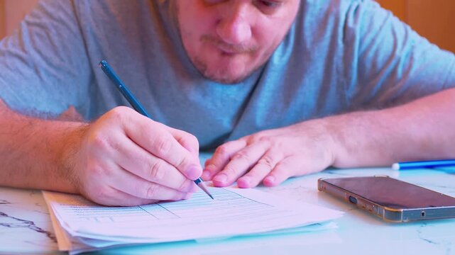 Close-up of a man filling out a paper document with a pencil.home office.cinematic shot of a middle-aged man carefully writing with a pencil on a form or draft at a desk under natural light.