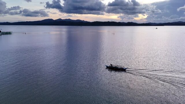 Drone shot of a fisherman casting a crab trap from a moving outrigger boat on the calm waters of Malampaya Sound, Philippines