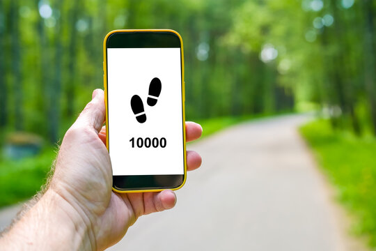 Hand holds smartphone with 10000 steps on forest road, concept of walking goal, fitness tracking and active lifestyle