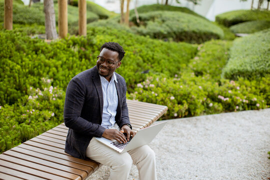 Man sits on bench working on laptop in garden during sunny day