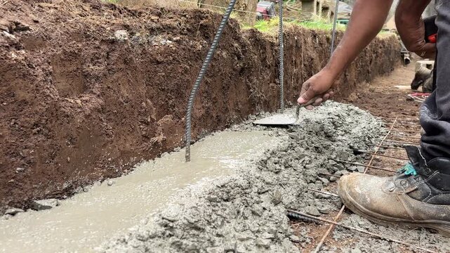 Construction worker smoothing concrete foundation trench with a trowel