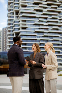 Business meeting with three people outdoors in a city setting near modern buildings