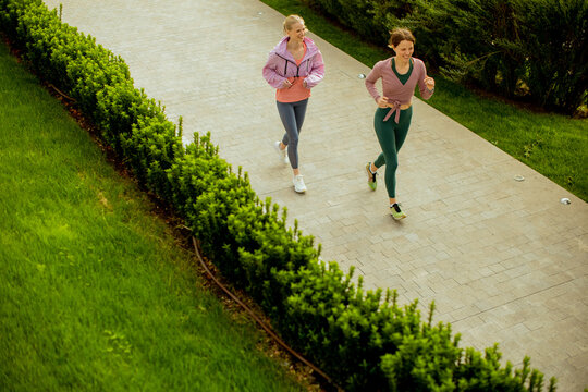Women run on a path in a green park during the day