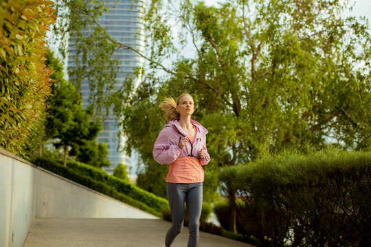 Young woman runs in urban park during morning hours near tall buildings