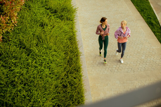 Two women run together on a path in a park during the morning
