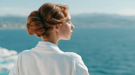 Fototapeta premium Serene woman with auburn hair in a robe enjoys a peaceful moment by the ocean