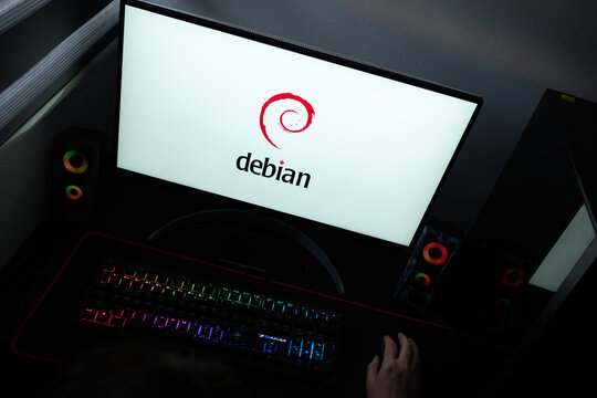 Punta Arenas, Chile &ndash; June 12, 2026: The official red swirl Debian Linux logo and text displayed on a computer screen in a dark room workspace setup