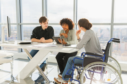 Teamwork brainstorm. Diverse multiracial colleagues woman in chair for people with disability working together. Group of people sitting in creative office discussing business. Young professional team