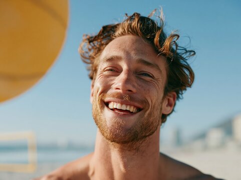 Joyful man with freckles laughing on a sunny beach with a yellow ball