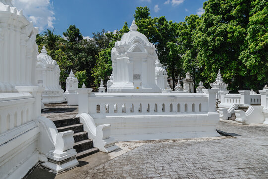 White stupas and lush green trees under a blue sky at Wat Suan Dok in Chiang Mai, Thailand. This Buddhist temple is a significant historical site.